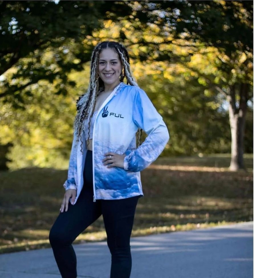 Woman posing outdoors in a blue and white jacket with tree-lined park background.