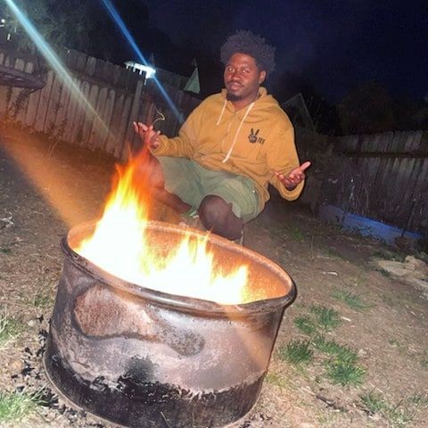 Person sitting near an outdoor fire pit at night, with flames illuminating the scene.