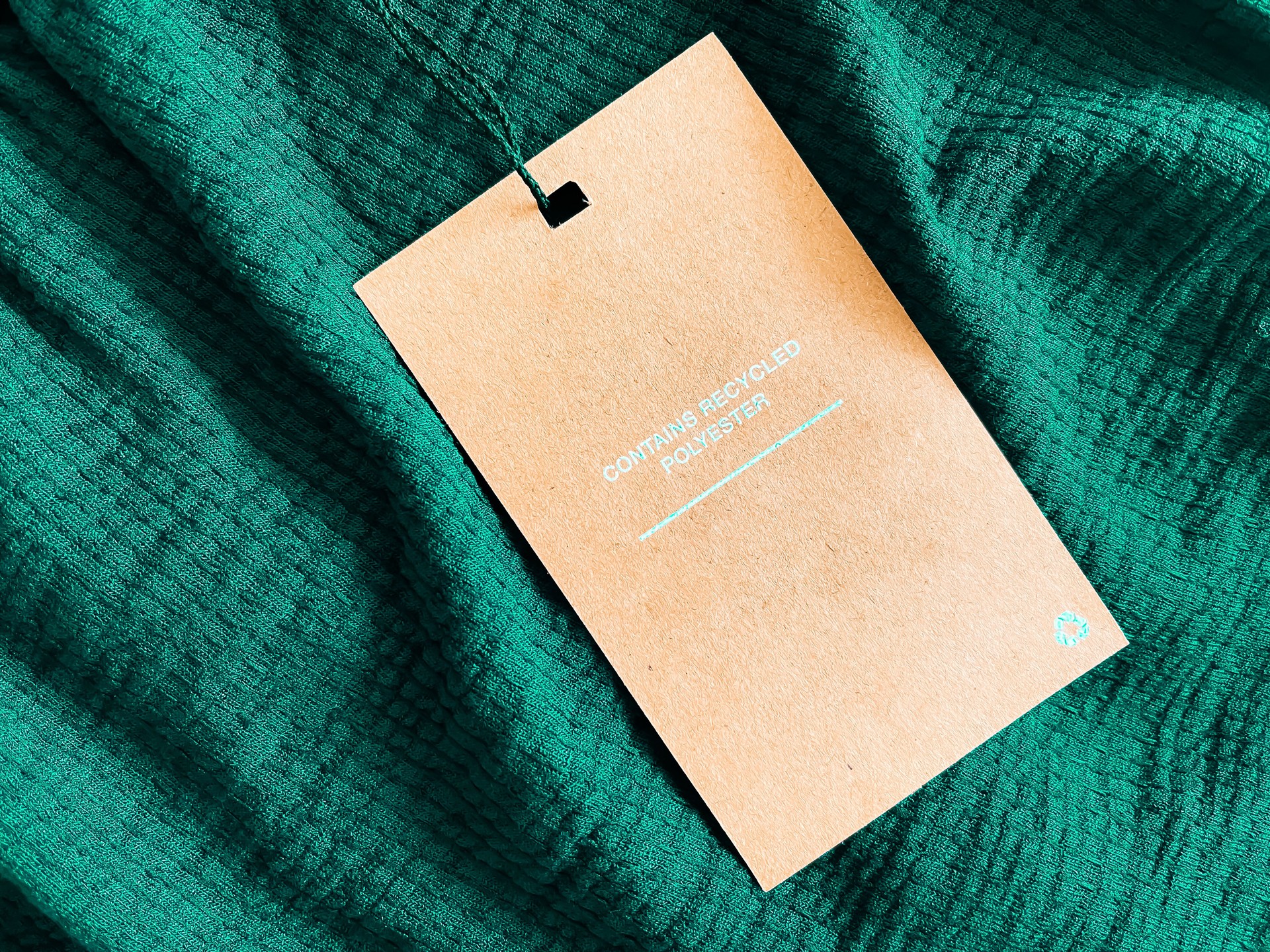 Contains recycled polyester fashion label tag, sale price card on luxury emerald green fabric background, shopping and retail