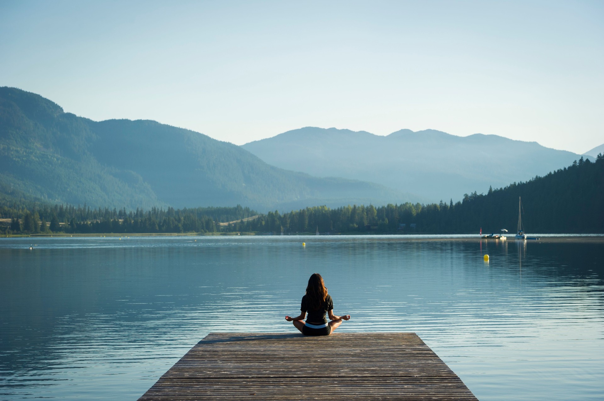 Young woman in lotus position on dock over lake